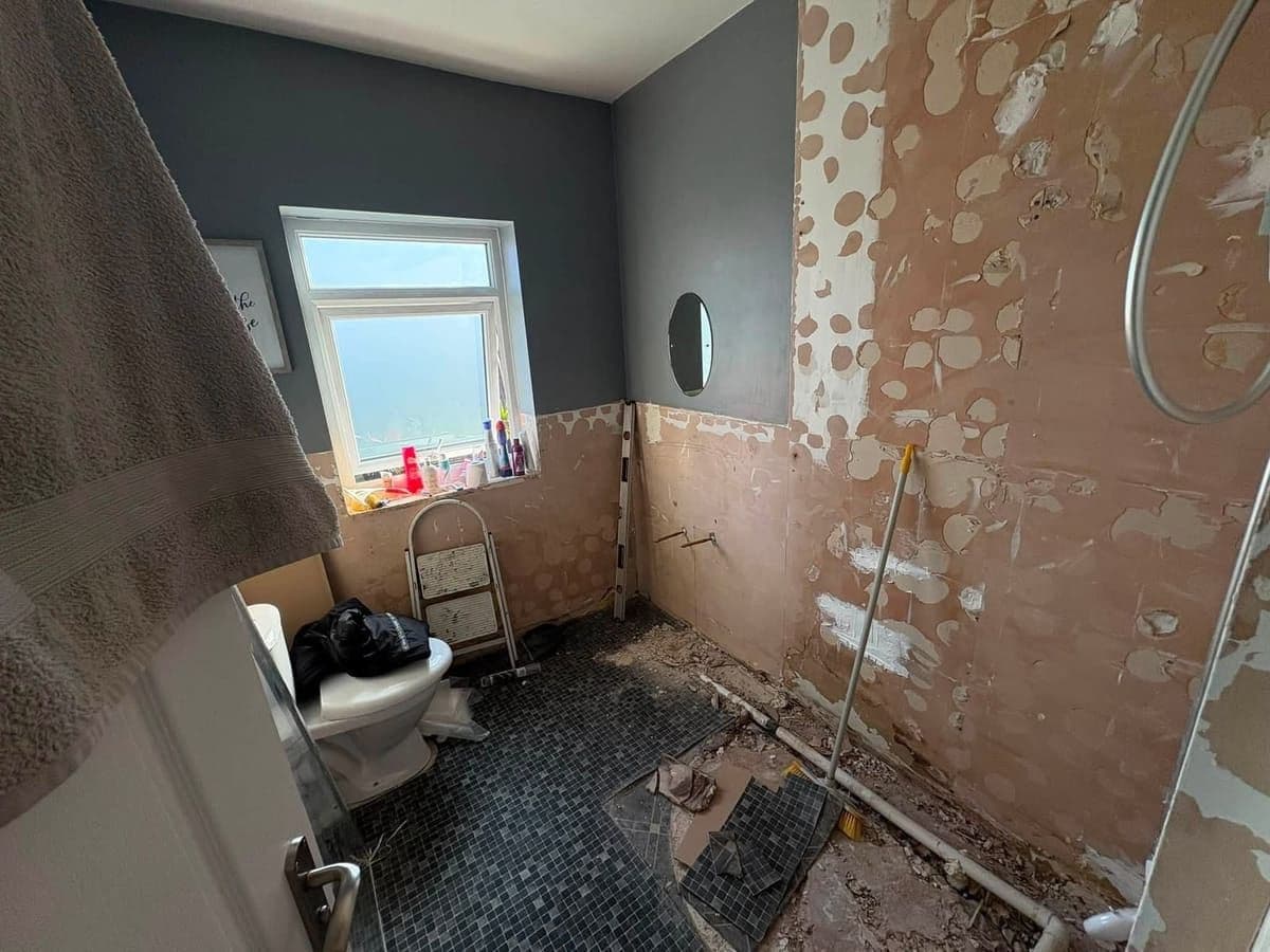 Old bathroom mid strip-out, tiles coming off the walls